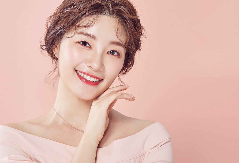 분홍 어깨 드러난 블라우스를 입고 한 손을 턱에 댄 채 활짝 웃는 업스타일 머리 모델