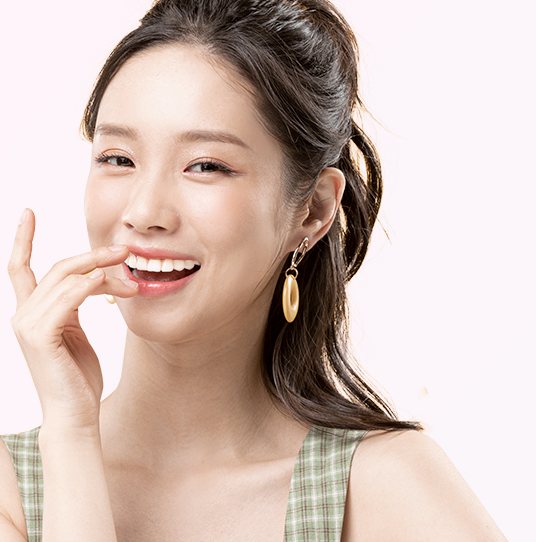 연분홍 바탕, 묶은 머리에 귀걸이를 한 모델이 손가락을 입가에 대고 활짝 웃는 모습