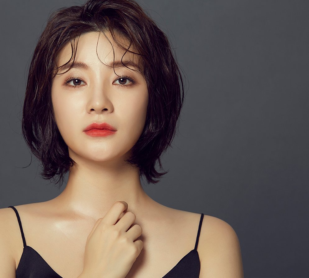어두운 회색 바탕, 젖은 듯한 단발머리에 붉은 입술의 모델이 한 손을 목에 댄 모습